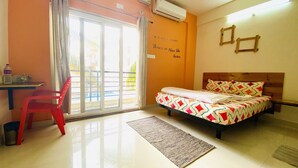 A hotel room with a bed, a desk, a chair, and a view of the outside. - Mapletree Inn (Bengaluru)