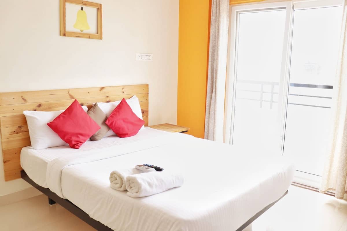 Ein Hotelzimmer mit einem hölzernen Kopfteil, weißer Bettwäsche, roten Kissen, einem aufgerollten Handtuch und einem gerahmten Bild an der Wand.