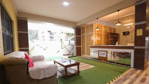 A hotel lobby with a sofa, a small table, a reception desk, and a view of the street through large windows. - Mapletree Inn (Bengaluru)
