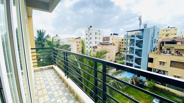 A balcony with a tiled floor and metal railing, overlooking a residential area with multi-story buildings and a clear sky. - Mapletree Inn (Bengaluru)