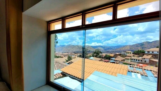 Una habitación con un amplio ventanal que ofrece vistas a un pueblo con tejados de teja y montañas en la distancia.