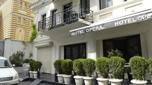 A hotel with a sign reading "HOTEL OPERA." It features a balcony with potted plants and a white car parked in front. - Hotel Opera (Tbilisi)