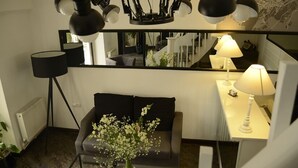 A modern living room with a sofa, a coffee table with flowers, a desk with a lamp, and a large mirror reflecting the room. - Hotel Opera (Tbilisi)