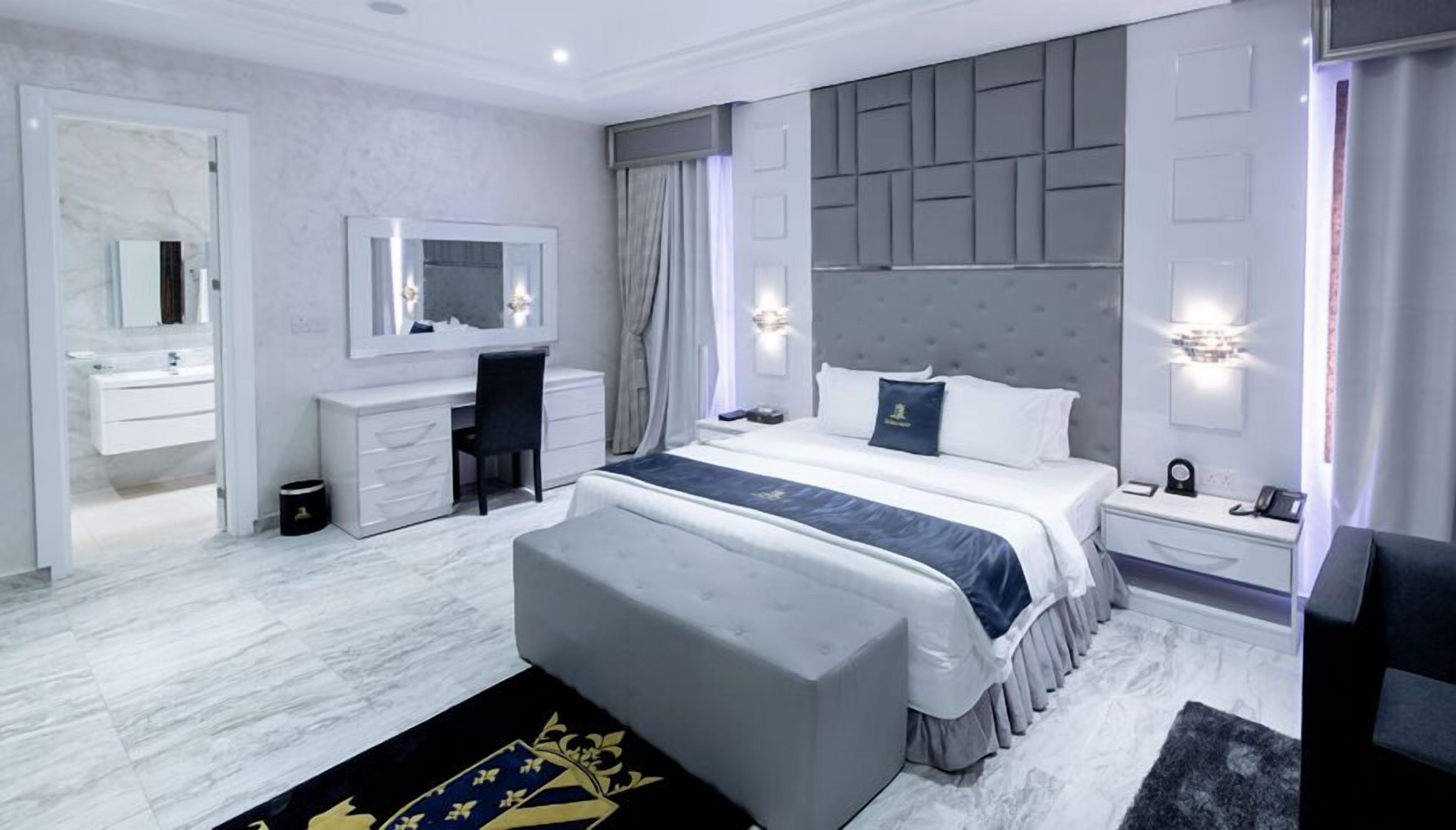 Una habitación de hotel moderna con una cama grande, un escritorio, una tocador y un espejo amplio.