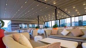 Un área de estar moderna con sofás, sillones, ventanas amplias y un techo con iluminación lineal.