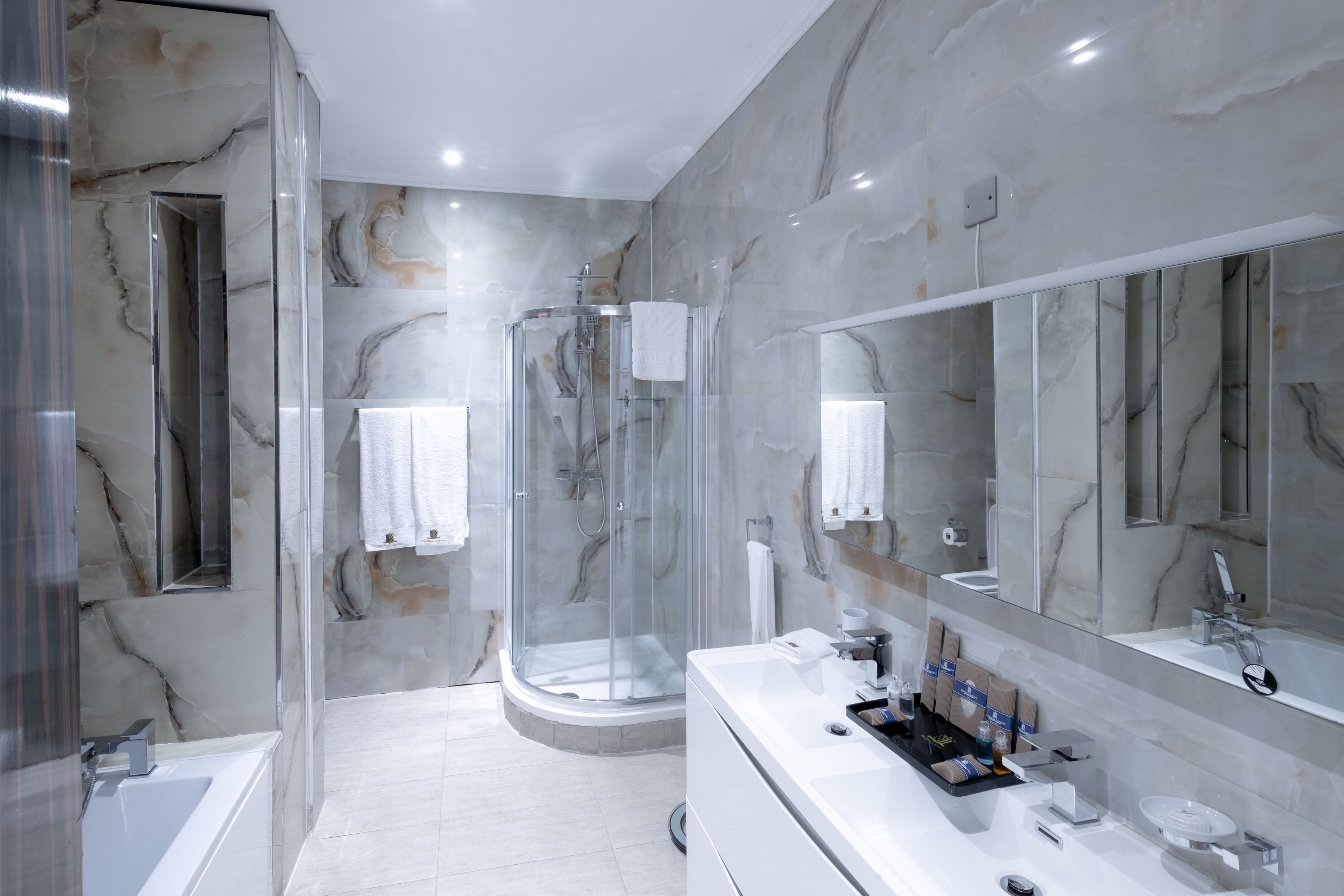 Een moderne badkamer met een douchecabine van glas, een grote spiegel en een witte wastafel met toiletartikelen.