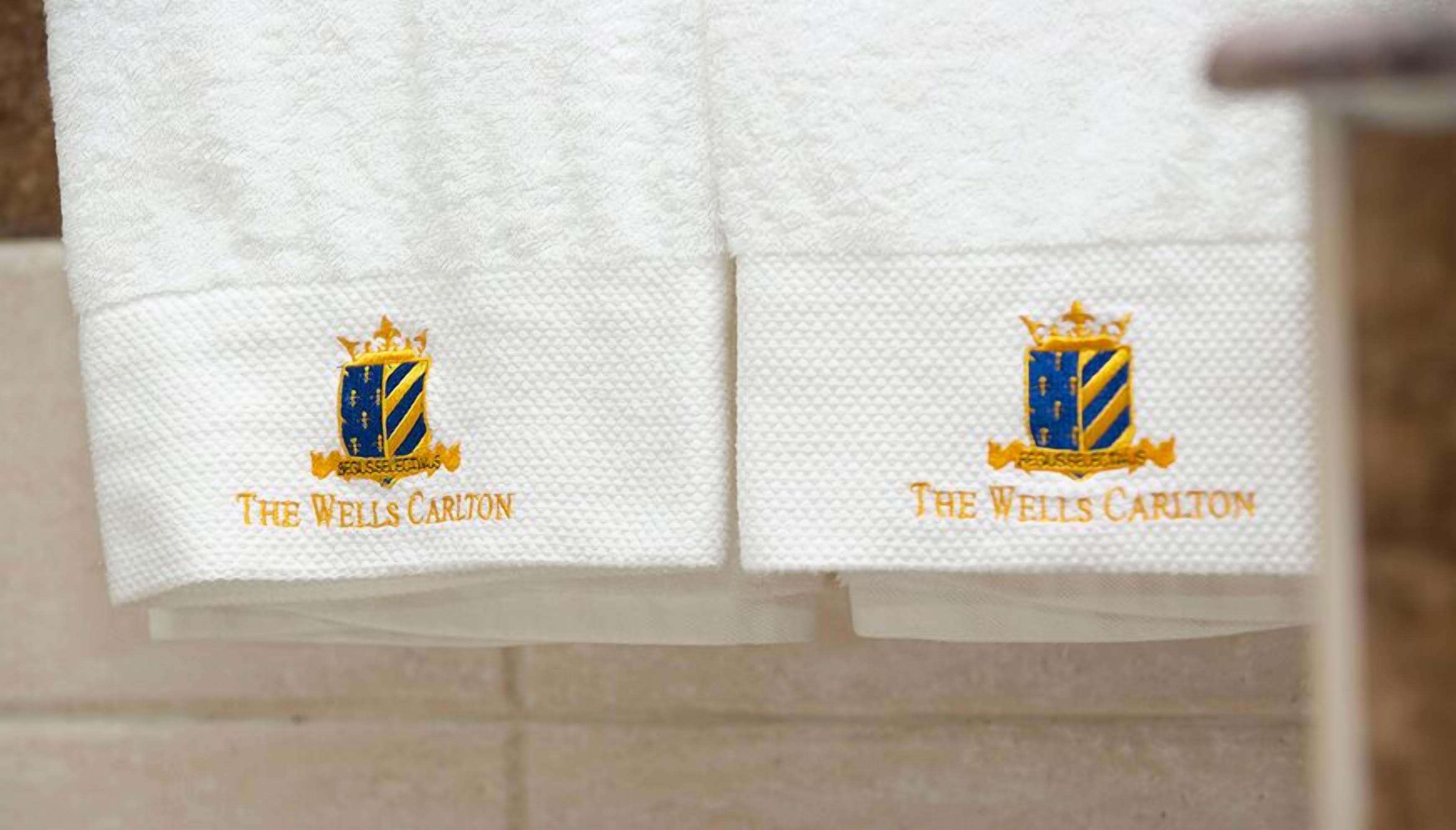 Dos toallas blancas con logotipos bordados y texto que dice "The Wells Carlton".