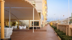 Un espacio al aire libre cubierto, con piso de madera, asientos blancos y una escalera que lleva a un nivel superior.