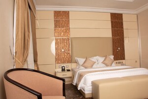 Une chambre d’hôtel avec un lit, des tables de chevet, une chaise et un grand miroir.