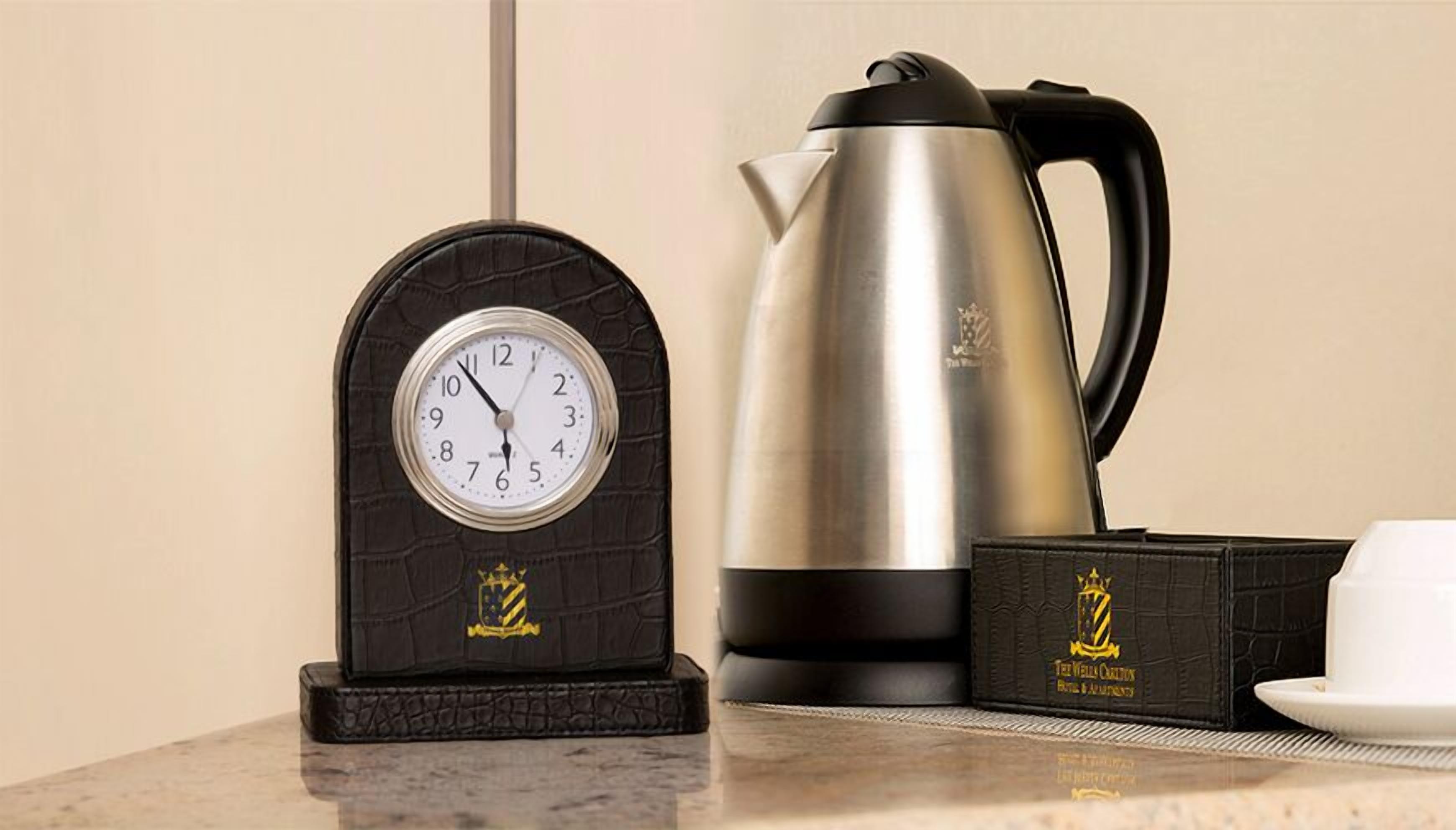 Un reloj de pared, una tetera de acero inoxidable y una caja de té sobre una encimera de mármol.