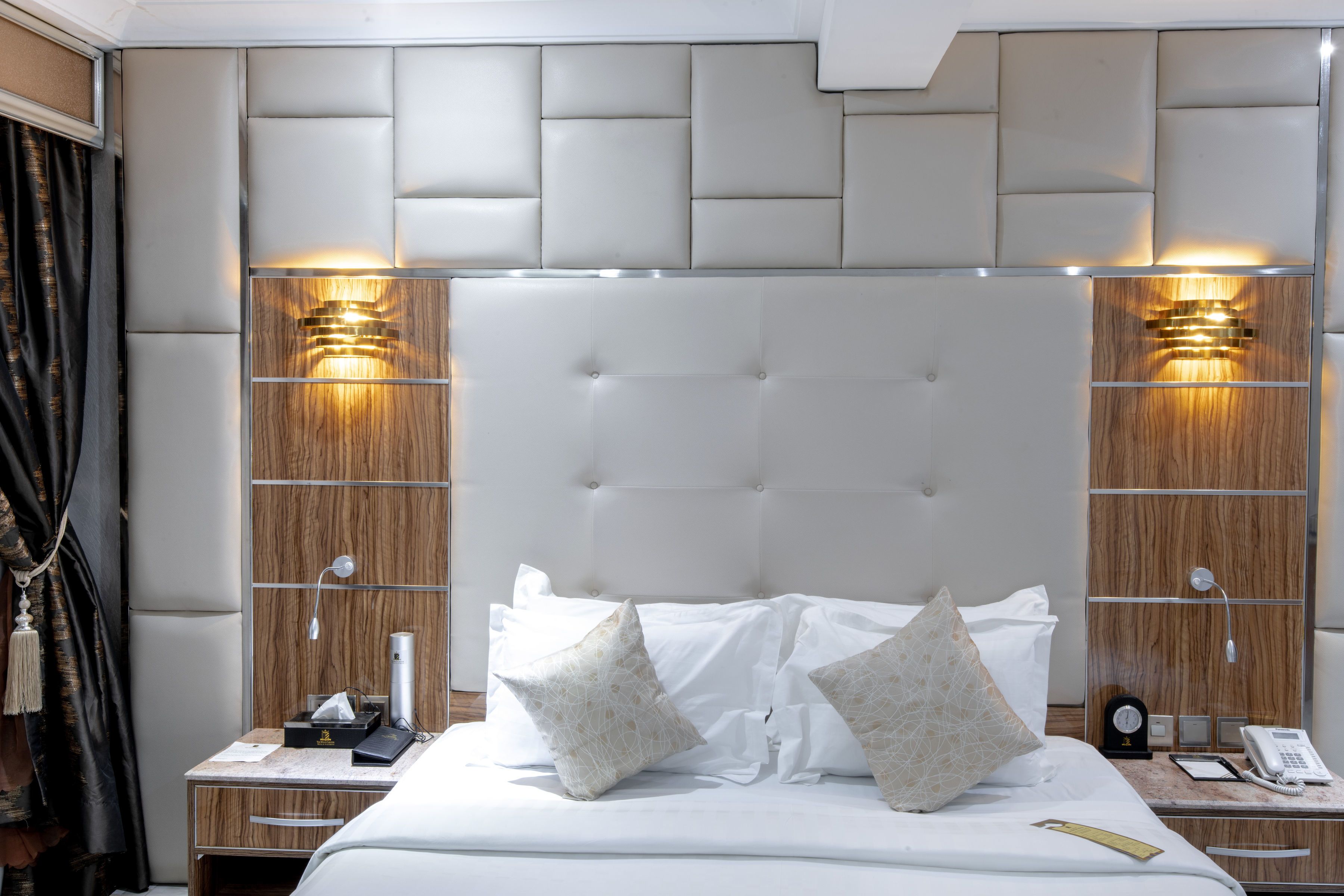 Une chambre d’hôtel avec un grand lit, deux tables de chevet, une tête de lit en bois et des lampes fixées au mur.