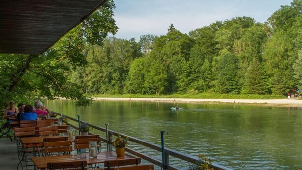 A lakeside restaurant with wooden tables and benches, surrounded by a forested area. - Munich Camping Glamping and Dorms (Munich)