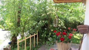 A garden with a wooden trellis, a wicker basket with red flowers, and a hanging lantern. - Landhaus Am Arzbach (Wackersberg)