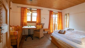 A cozy room with a wooden ceiling, a bed, a sofa, a table, and a chair. - Landhaus Am Arzbach (Wackersberg)