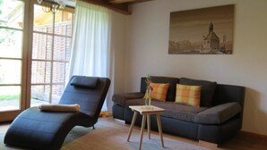 A living room with a dark-colored sofa, a recliner, and a small wooden table with a vase. - Landhaus Am Arzbach (Wackersberg)