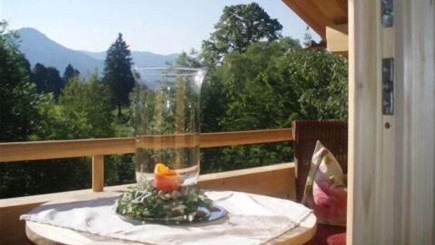 A wooden deck with a table, a glass vase with a flower, and a mountain view. - Landhaus Am Arzbach (Wackersberg)