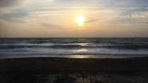Une plage où le soleil se couche sur l’océan, les vagues déferlent sur le rivage et le ciel est dégagé.