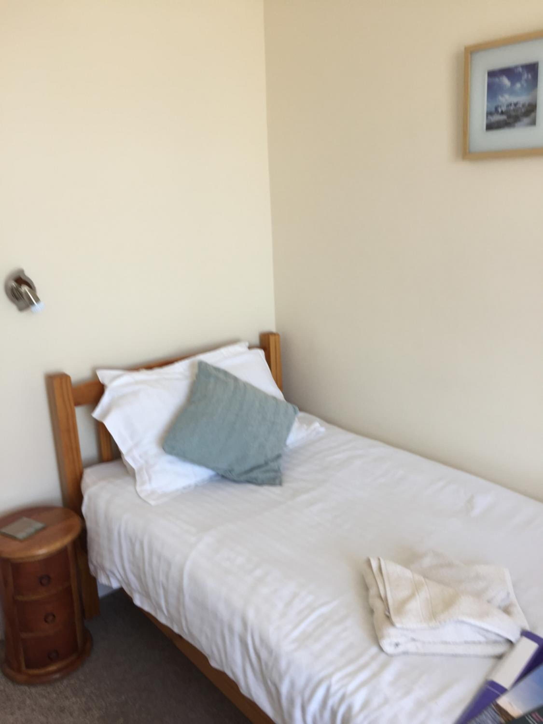 Una cama individual con cabecera de madera, una mesita de noche y un cuadro enmarcado en la pared.
