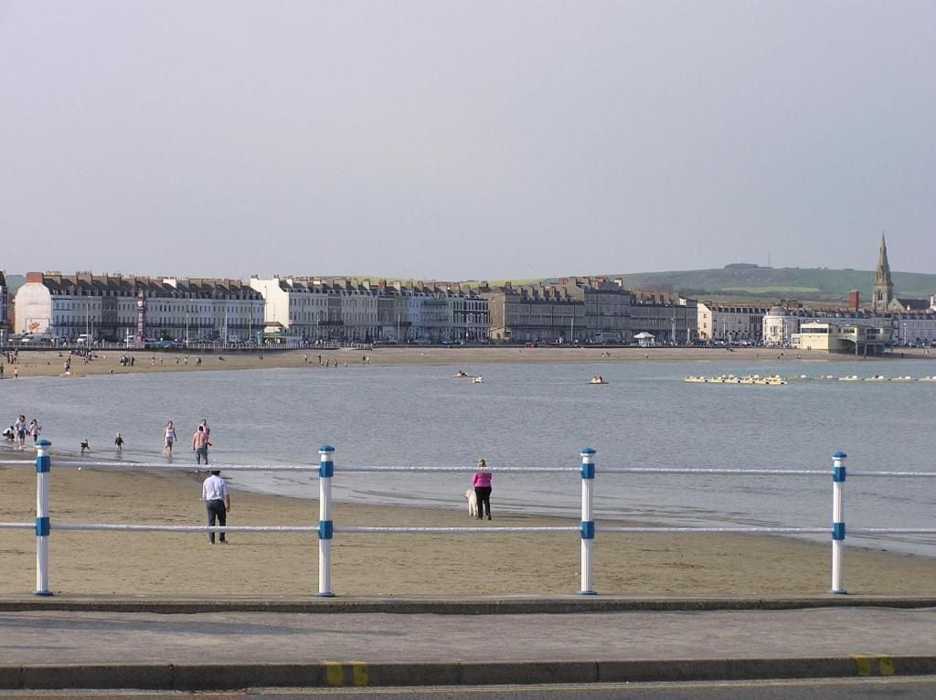 En strandpromenad längs kusten med en rad byggnader, en strand och en pir.