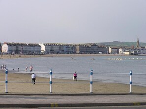A coastal promenade with a row of buildings, a beach, and a pier. - The Beach House (Weymouth)