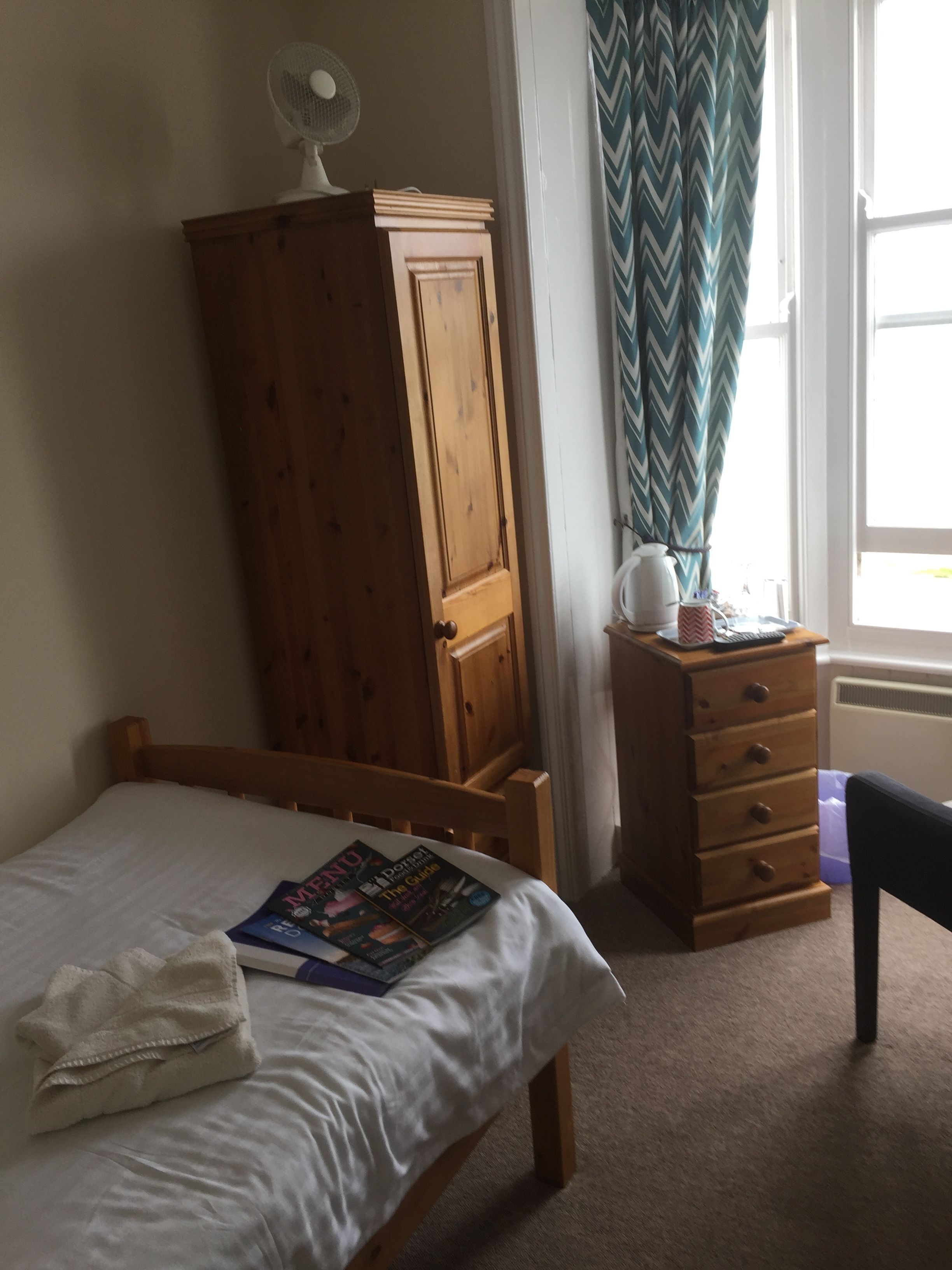 A bedroom with a wooden bed, a wooden wardrobe, a bedside table with a lamp, and a window with curtains.