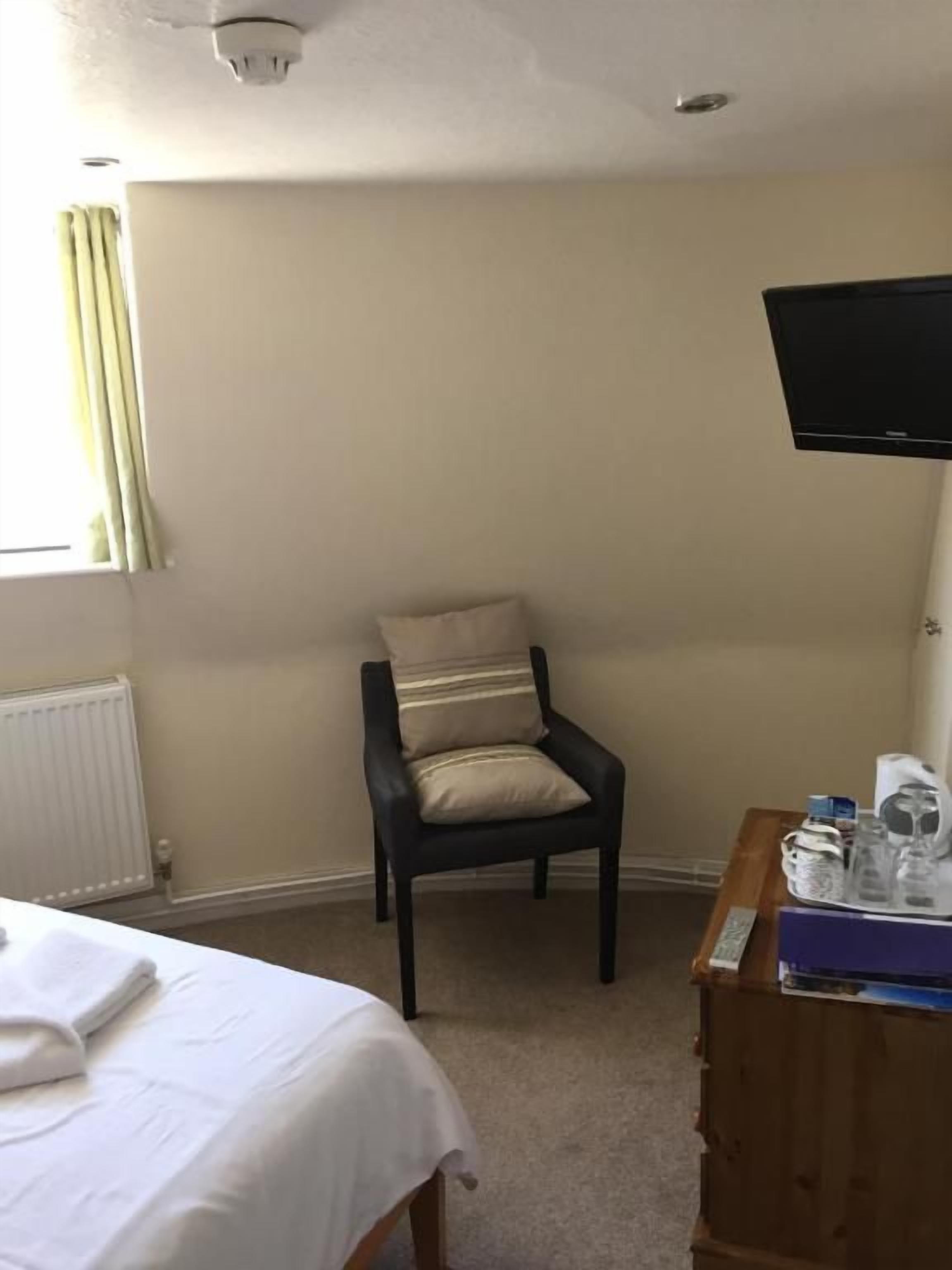 A hotel room with a bed, a chair, a television, and a wooden dresser.