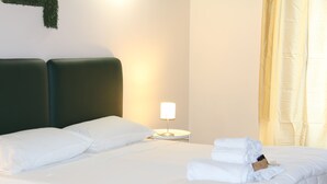 A neatly made bed with white linens and pillows, a bedside lamp, and a folded towel on the bed. - Urban Pop Hostel & BnB (Catania)