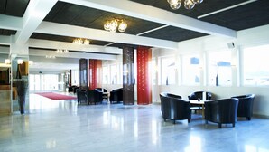 Tilava aula, jossa on modernit kattokruunut, punainen matto ja mustat nahkaverhoillut istuimet.