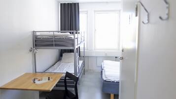 Un dormitorio con literas, una mesita, una silla y un ventanal con cortinas.