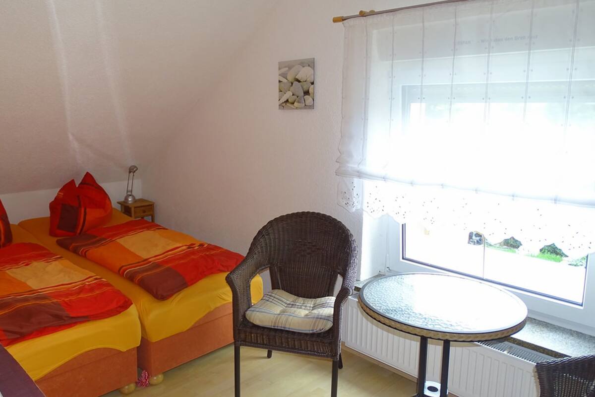 A room with two beds, a chair, a small table, and a window with a view.