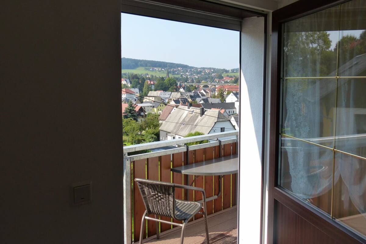 A balcony with a table and chair, offering a view of a town with houses and a bridge.