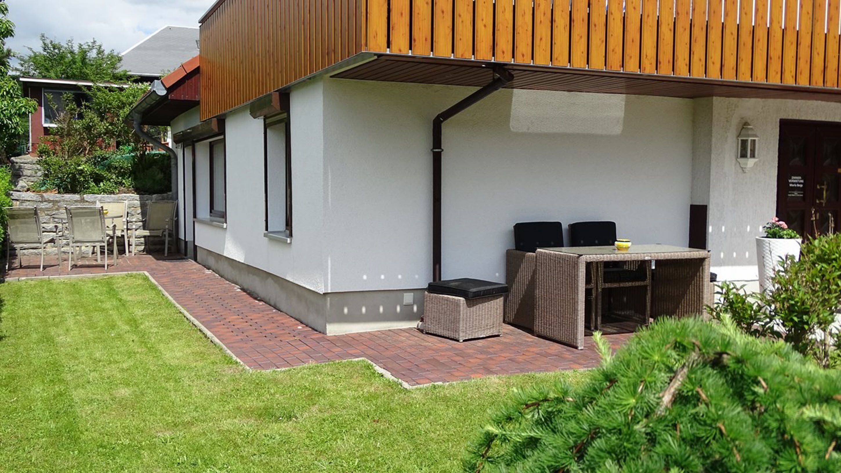 A modern outdoor patio with a brick pathway, a wooden pergola, and a dining area with wicker furniture.