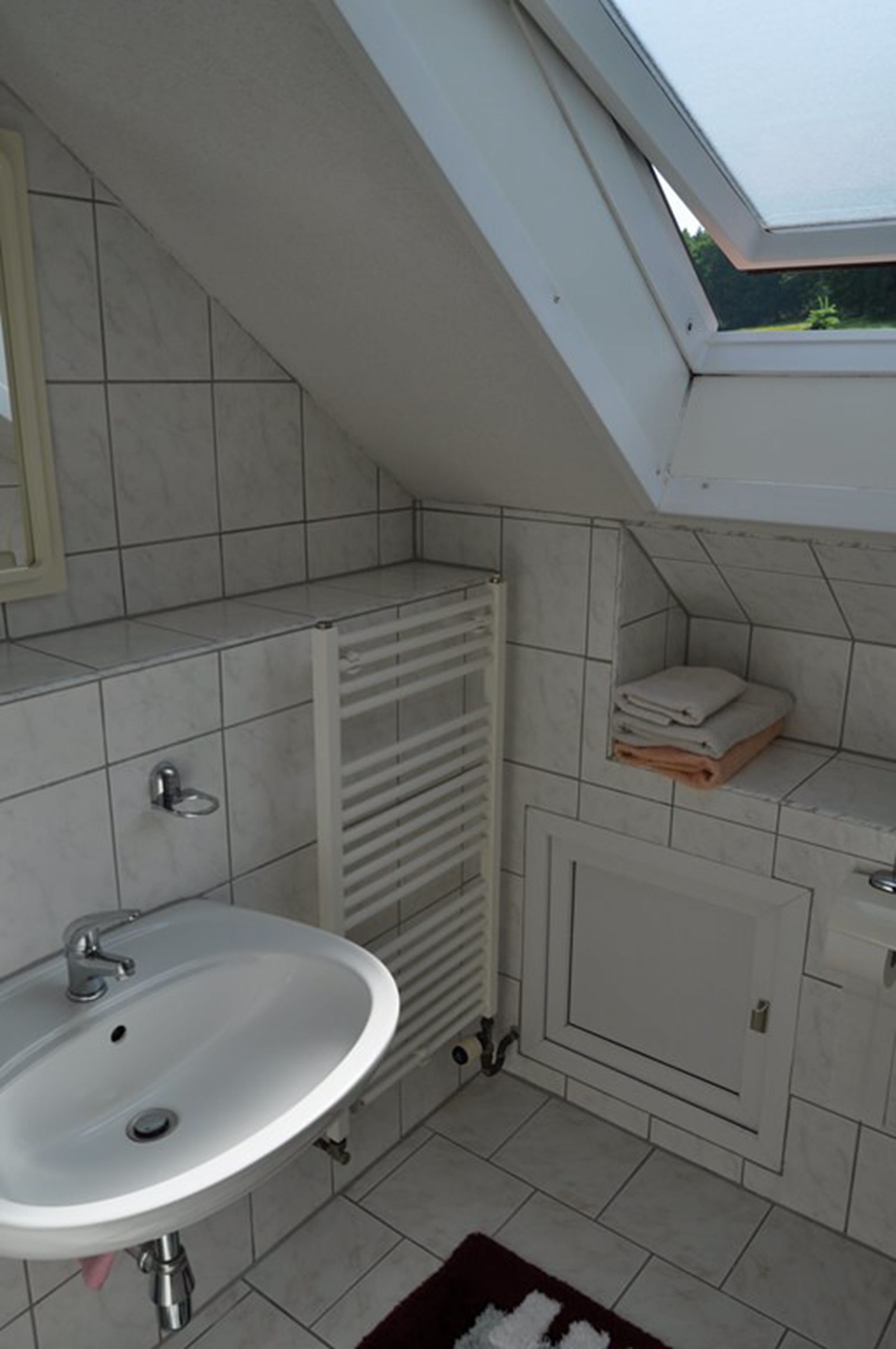 A bathroom with a skylight, a sink, a towel rack, and a radiator.