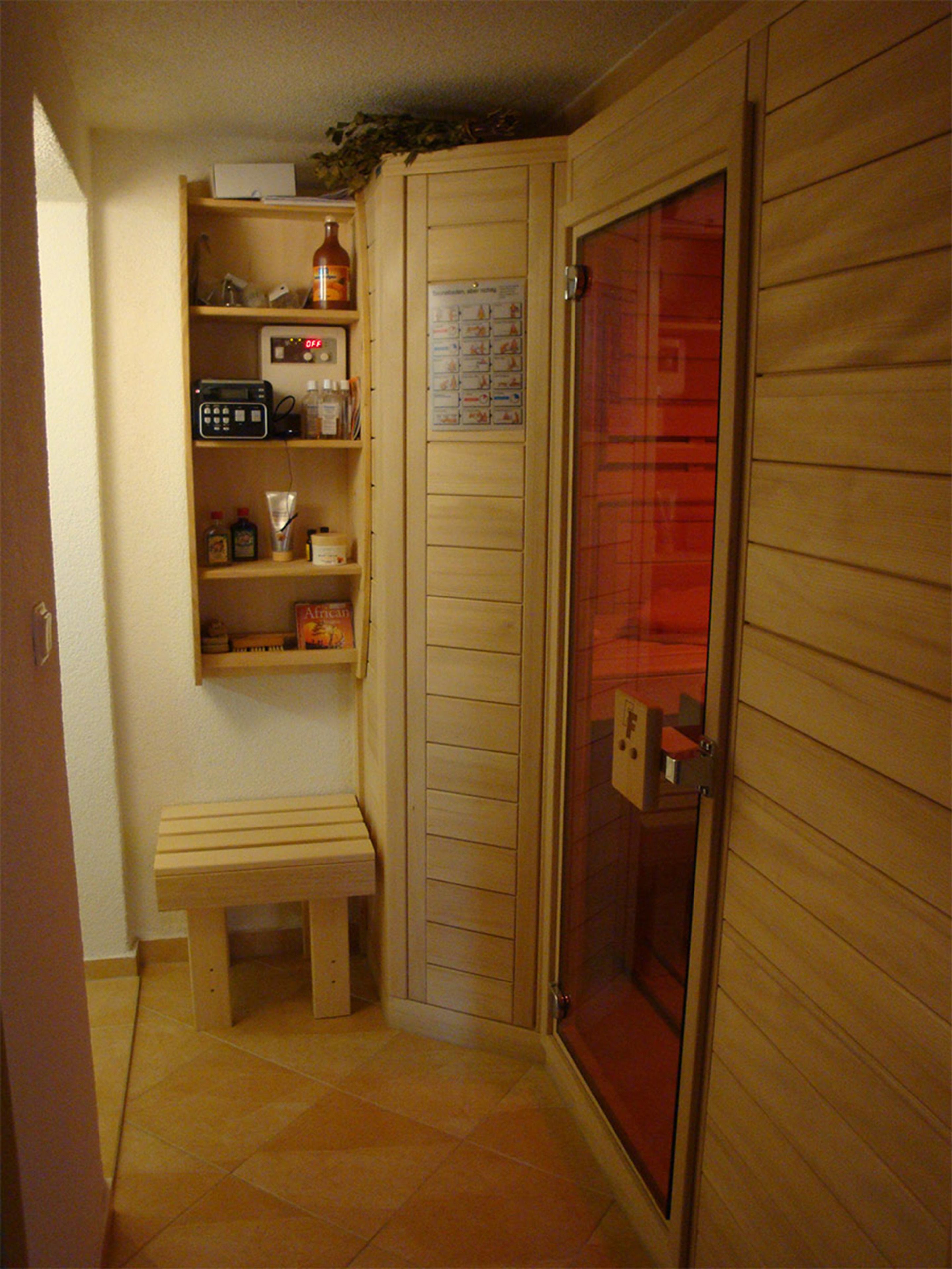 A small room with a wooden bench, a shelf with various items, and a door with a red glass panel.