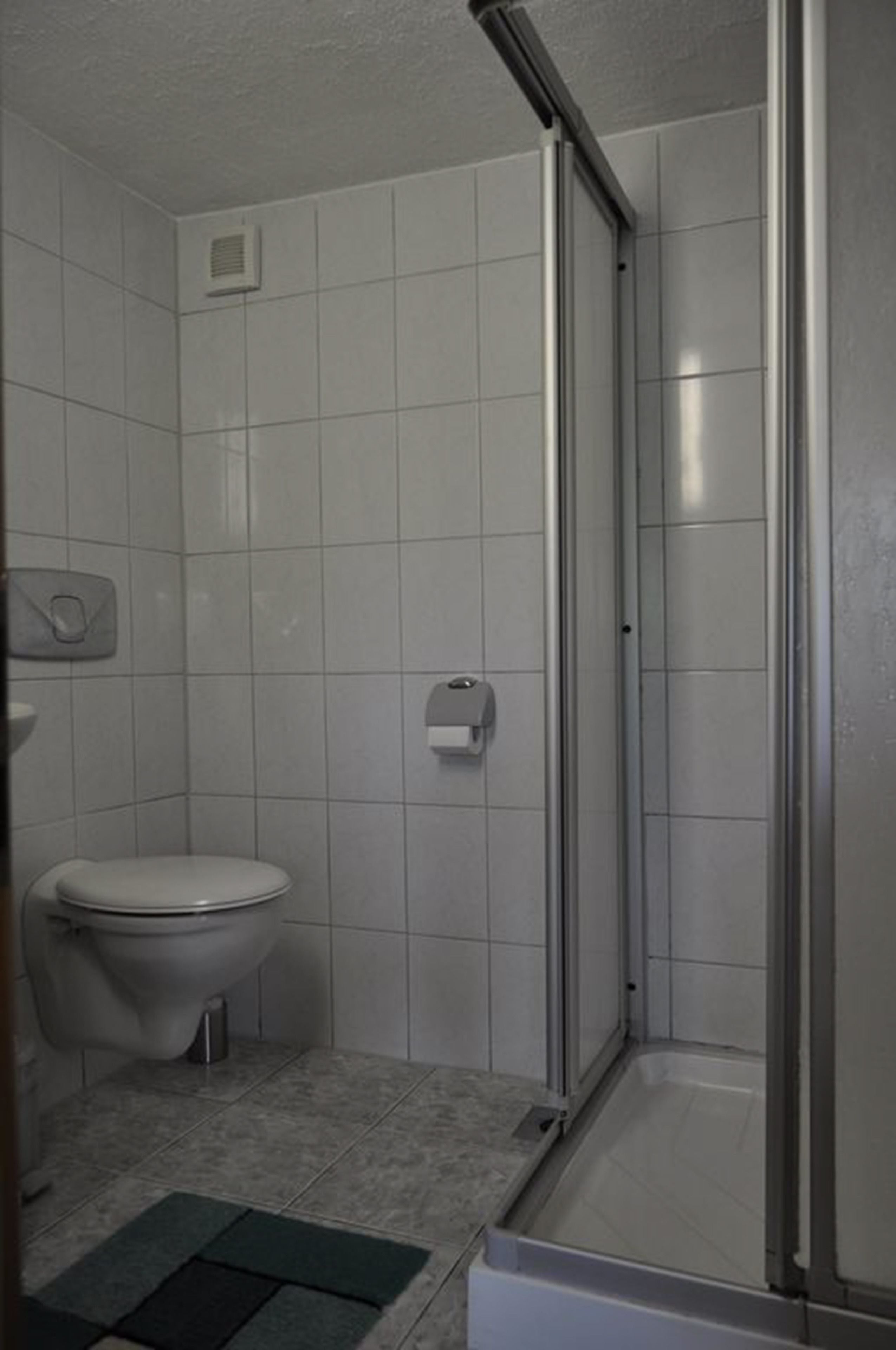 A small bathroom with a toilet, a hand dryer, and a shower stall.