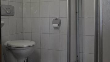A small bathroom with a toilet, a hand dryer, and a shower stall.