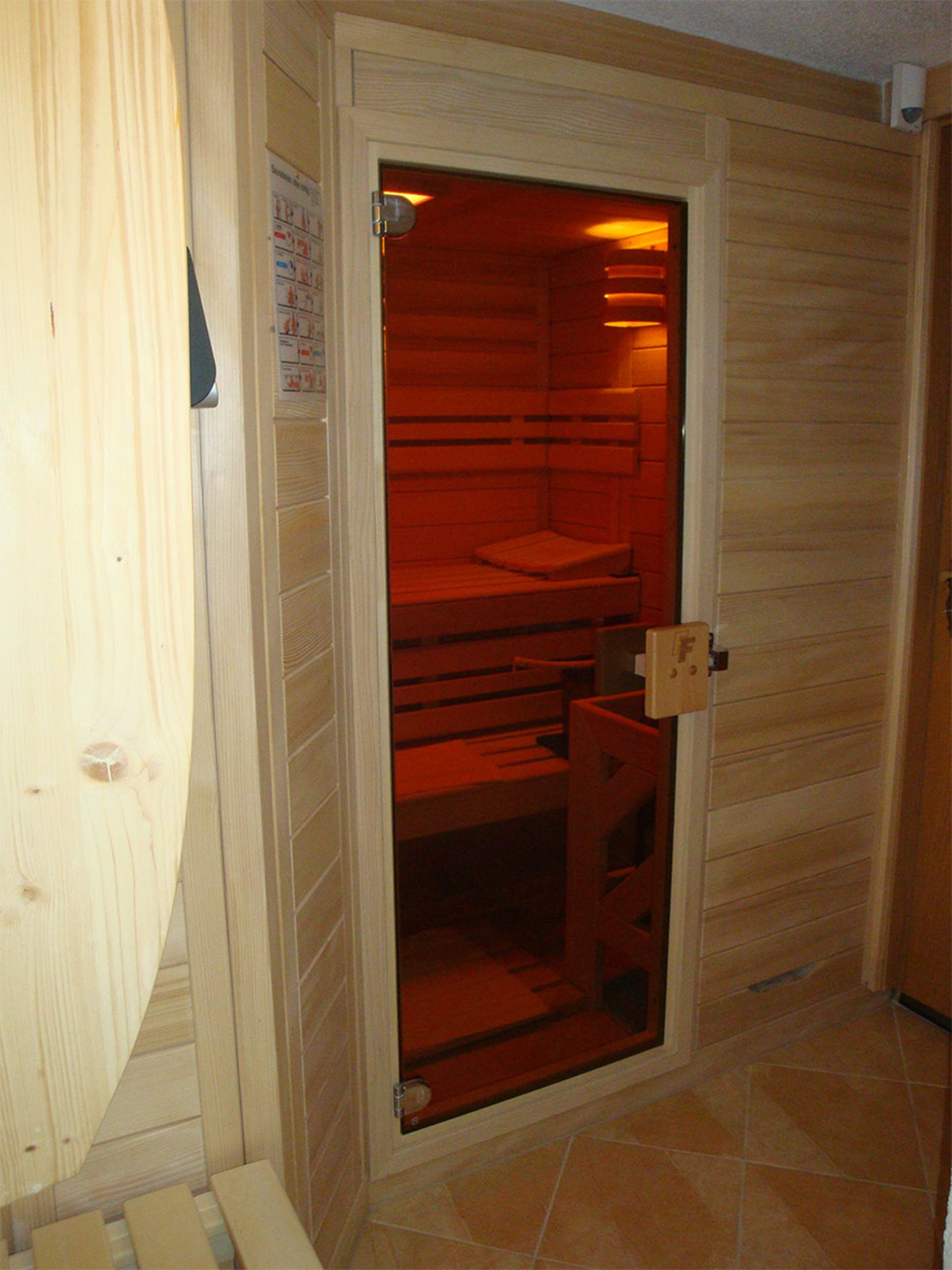A sauna room with wooden walls and a glass door.