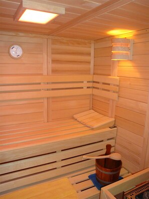 A sauna with wooden benches, a wooden bucket, and a wall-mounted clock. - Gästezimmer & Ferienwohnung Berge (Schirgiswalde-Kirschau)