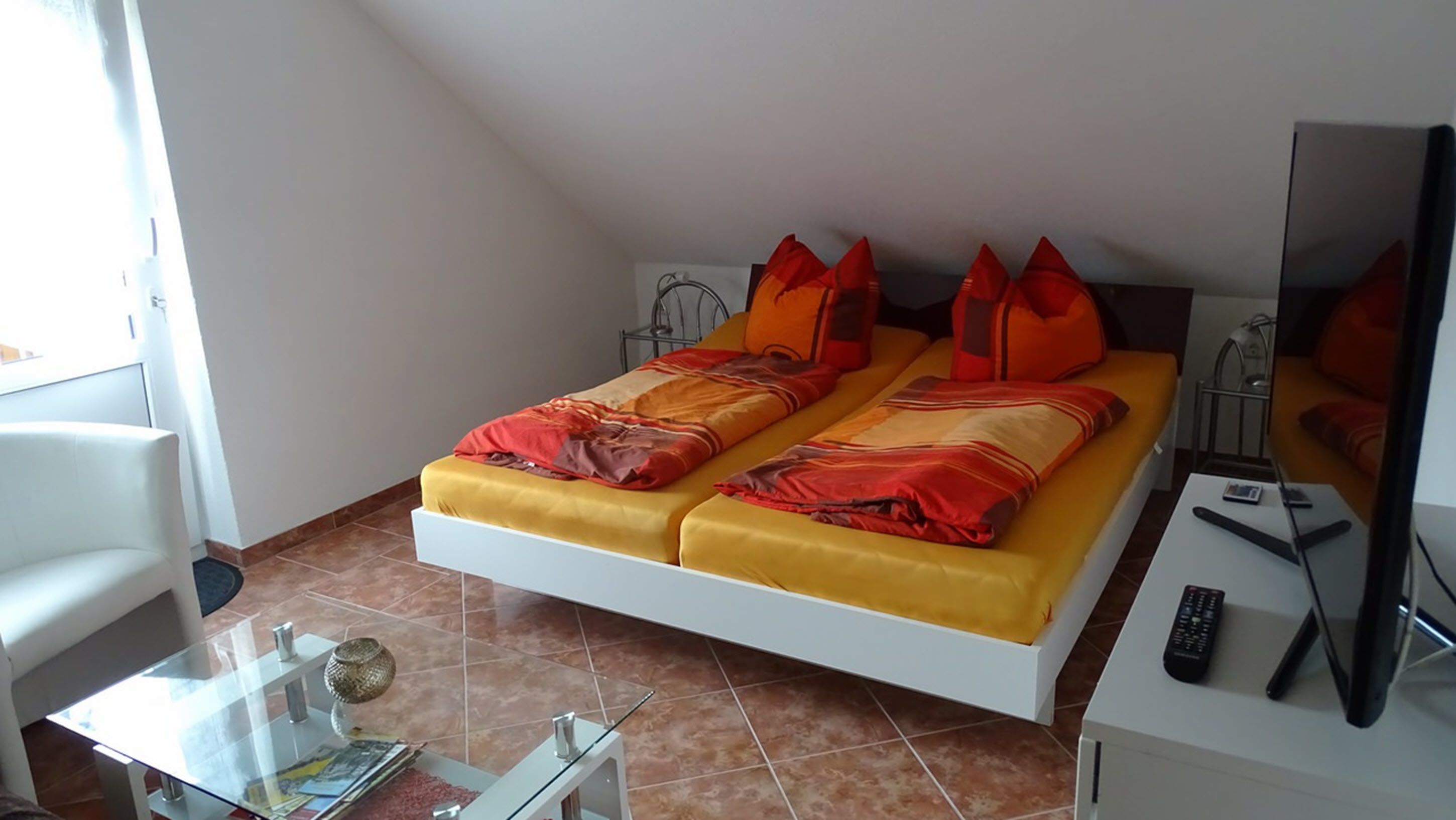 A hotel room with a bed, a TV, a glass table, and a chair.