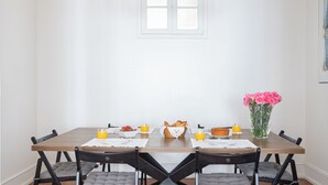 Une table à manger dressée avec des aliments pour le petit-déjeuner, un vase de fleurs et une fenêtre au-dessus.