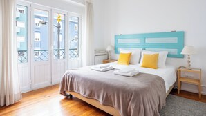 Une chambre à coucher avec un lit, une table de chevet, une lampe et une vue sur les immeubles par la fenêtre.