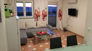 A living room with a sofa, a glass coffee table, and a TV mounted on the wall. - Apartments Michael (Omisalj)