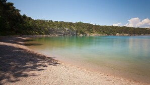 A beach with clear water, a sandy shore, and a forested hillside in the background. - Apartments Michael (Omisalj)