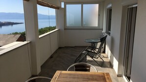 A balcony with a table and chairs, a view of the sea, and a window. - Apartments Michael (Omisalj)