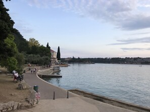 Un paseo junto al río con un muro de piedra, bancos y un cartel de prohibido fumar.