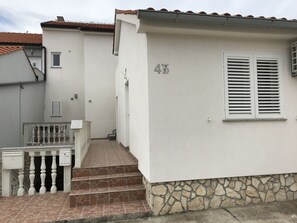 Un edificio blanco con base de piedra, número 45, que presenta una escalera que conduce a una puerta con un pequeño ventanal.
