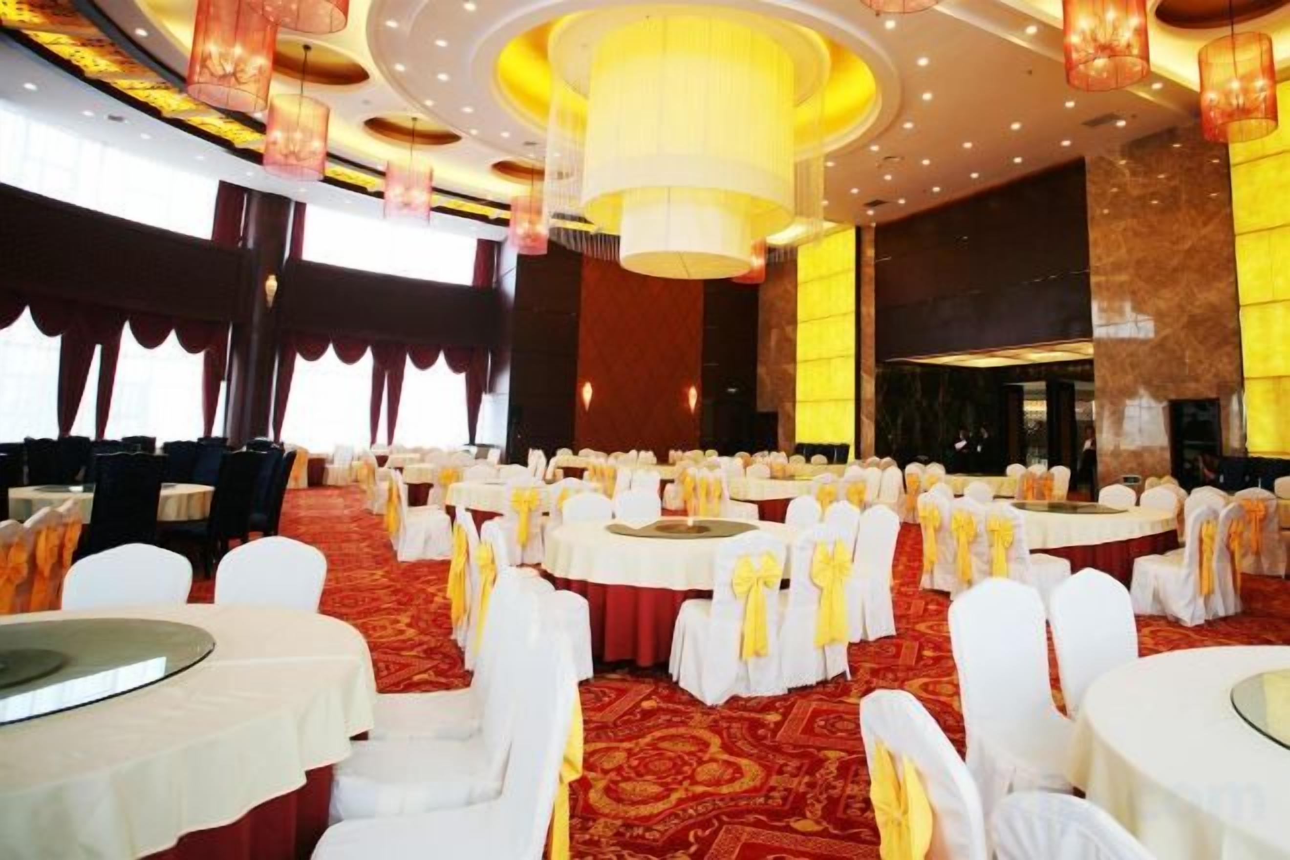 A banquet hall with round tables and chairs, a red carpet, and a chandelier.