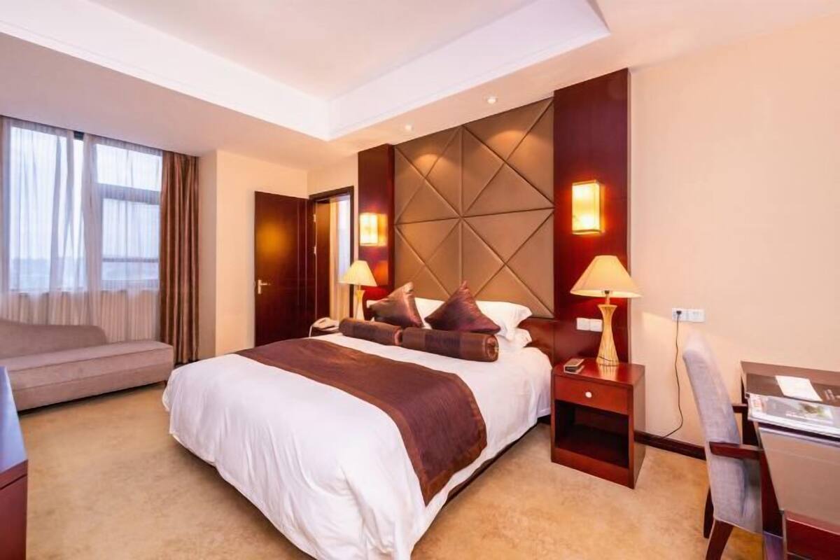 Quarto de hotel com uma cama grande, duas mesas de cabeceira com luminárias, uma escrivaninha e um sofá.