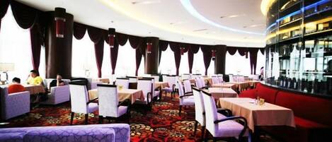 Restaurante com mesas e cadeiras redondas, carpete estampado e um espaço de bar.