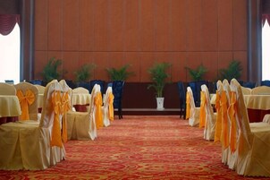 Un salón de conferencias con filas de mesas y sillas, alfombra roja y plantas en macetas.